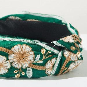 Detailed close-up of dark green knotted headband with intricate floral embroidery and sequins