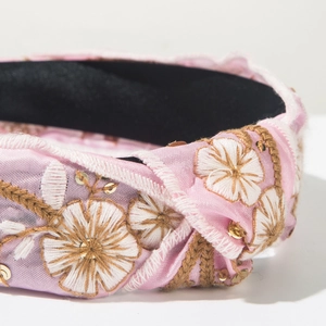 Detail of pink satin headband featuring white daisy embroidery and gold sequins