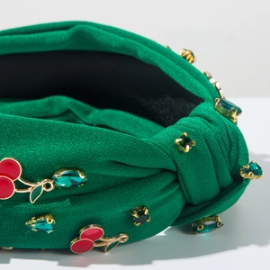 Détail d'un bandeau noué vert avec strass en cristal et breloques de cerises rouges