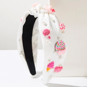 Dettaglio del cerchietto in tessuto bianco con perle e accessori a forma di caramelle