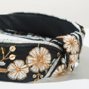 Detail of hand-embroidered floral patterns and golden sequins on a knotted fabric headband