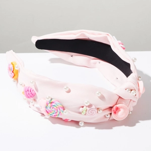 Dettaglio di cerchietto rosa in tessuto con perle sintetiche e decorazioni a forma di caramella