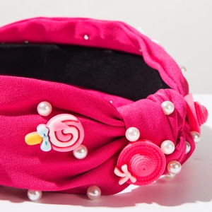 Dettaglio del cerchietto in tessuto fucsia con perle bianche e ciondoli a caramella