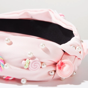 Dettaglio cerchietto in tessuto rosa annodato con perle e decori a caramella
