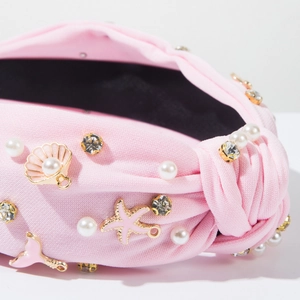 Detail van roze geknoopte hoofdband met parels, strass en oceaan bedeltjes