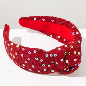 Detailed view of red knotted wide headband with glittering sequins and festive snowflake patterns