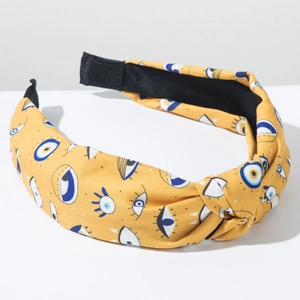 Close-up of mustard yellow wide headband featuring blue evil eye patterns and cross knot
