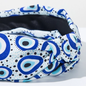 Detail of fabric headband featuring blue evil eye pattern and elegant knotted design