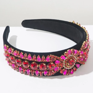 Detail of red rhinestone clusters and gold settings on a black velvet wide headband