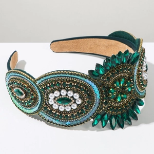 Close-up of luxury Baroque headband with emerald rhinestones and white pearls on velvet