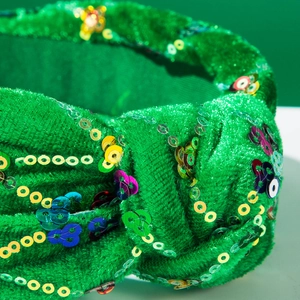 Gros plan du serre-tête en velours vert avec paillettes colorées et nœud central
