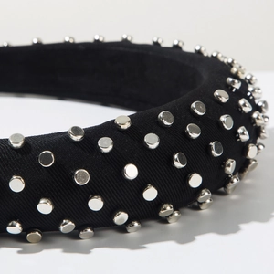Dettaglio del cerchietto imbottito nero con borchie metalliche e trama in tessuto twill