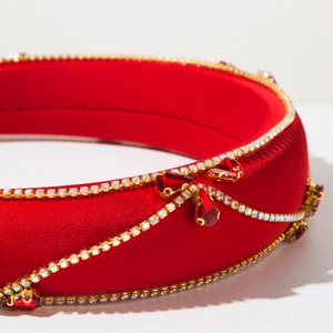 Close-up of red satin headband with rhinestone chain and faux gemstone details