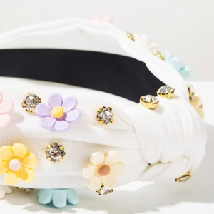 Close-up of white knotted headband with candy color plastic flowers and shiny rhinestones