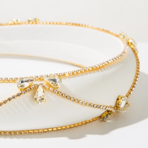 Close-up of white satin headband with gold chains, crystals and bow pendant details