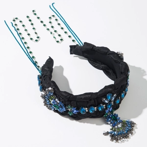 Détail d'un serre-tête en tissu noir avec strass émeraude et pompons métalliques