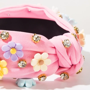 Detail of pink knitted headband featuring knotted fabric, colorful resin flowers and rhinestones