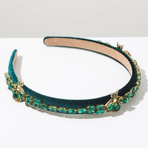 Detailed close-up of a green velvet headband with gold bee accents and emerald gemstones