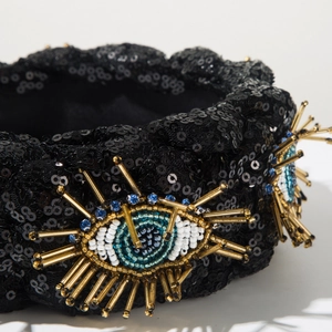 Makrodetail der handgenähten Evil-Eye-Perlenstickerei auf einem schwarzen Pailletten-Haarband