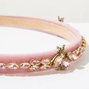Macro detail of pink velvet headband featuring crystal stones and a golden bee charm