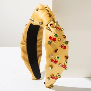 Détail d'un serre-tête en satin jaune avec breloques cerises et strass brillants