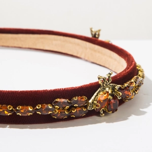 Macro detail of luxury burgundy velvet headband with amber crystals and golden bee