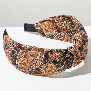 Close-up of bohemian wide headband featuring orange paisley patterns and top knot detail