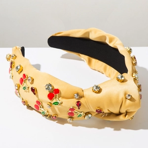Détail d'un serre-tête en satin champagne avec cerises en strass et nœud sur le dessus