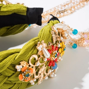 Detailansicht eines grünen Haarreifs mit goldenen Blumen und Perlenbesatz im Detail
