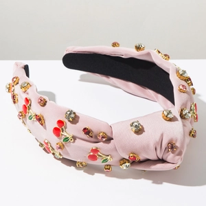 Détail du serre-tête en satin rose avec strass brillants et breloques cerises émaillées