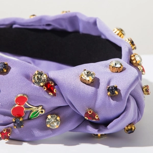Détail d'un serre-tête en satin violet avec strass en cristal et breloques cerise émaillée