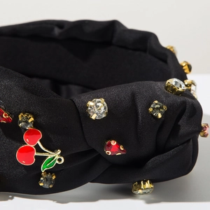 Détail d'un serre-tête en satin avec strass brillants et pendentif cerise rouge
