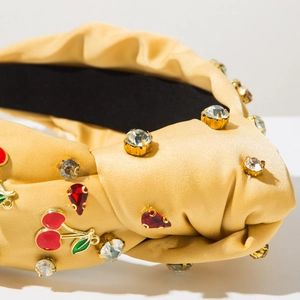 Détail du serre-tête en satin jaune avec des strass et un ornement de cerise rouge