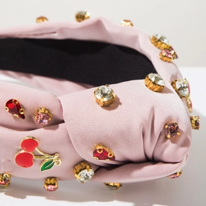 Détail du serre-tête en satin rose avec strass colorés et breloques de cerises