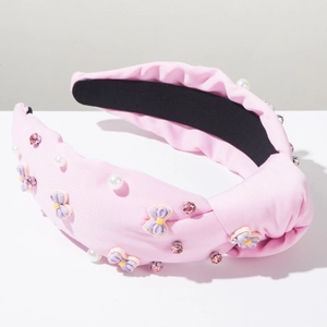 Dettaglio del cerchietto in tessuto rosa con fiocco viola, perle bianche e strass lucidi