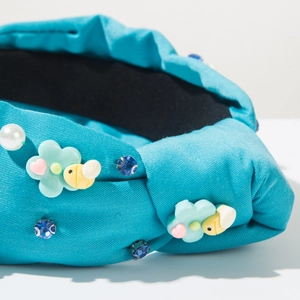 Dettaglio di un cerchietto blu con nodi, ciondoli a fiori, perle e strass blu