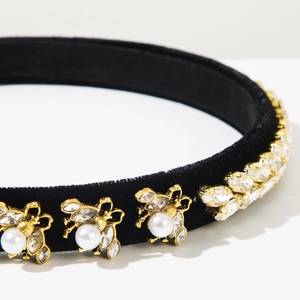 Close-up of golden bee ornament with crystals and pearl on black velvet headband
