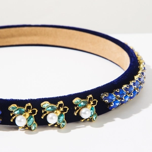Detailed macro view of blue velvet headband with gold bees and emerald crystal accents