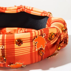 Detailed close-up of a knotted plaid headband with orange rhinestones and maple leaf charms