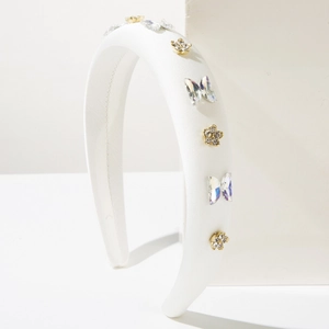 Détail d'un serre-tête en satin blanc avec papillons en cristal et fleurs dorées diamantées