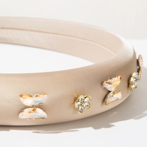 Détail macro du serre-tête en satin champagne avec papillon et fleurs en strass brillants