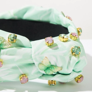 Nahaufnahme von mintgrünem Stoffstirnband mit bunten Kristallen und goldenem Schmetterling