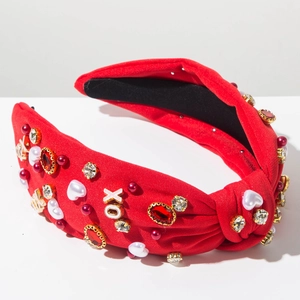 Detail van rode geknoopte haarband met strass parels en gouden XO-letter accenten op de stof