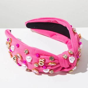 Detail van roze geknoopte hoofdband met XO-letters van strass en parelmoeren hartjes