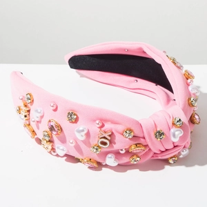Detail van roze geknoopte hoofdband met strassteentjes, parels en gouden XO-letters
