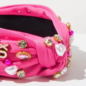 Detail van een roze geknoopte hoofdband met hartparels, strass en XOXO metalen bedeltjes