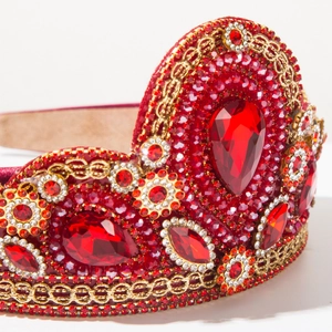 Detail van rode barokke tiara met fonkelende kristallen steentjes en gouden kettingen
