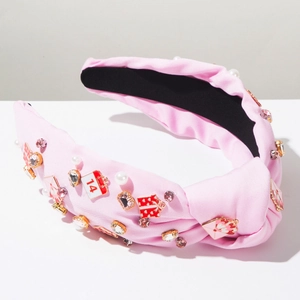 Close-up of pink knotted headband with heart, pearl, and enamel envelope charms