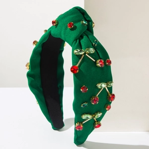 Dettaglio cerchietto in tessuto verde scuro con ciliegie di cristallo su supporto bianco