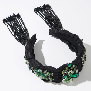 Detail eines handgewebten schwarzen Haarreifens mit grüner Strassblume und Quasten